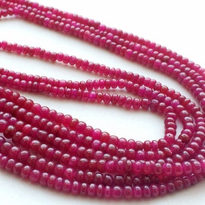 May include: A strand of deep pink ruby beads. The beads are round and smooth, and they are strung on a clear thread. The beads are arranged in a loose, flowing pattern.