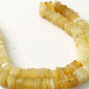 May include: A strand of yellow opal beads, each bead is a rectangular shape with a slightly rounded edge. The beads are strung on a clear thread.