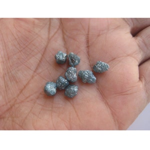 May include: A collection of small, rough, gray diamonds. The diamonds are scattered on a person's hand.