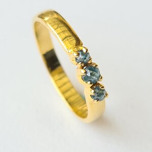 Può includere: Un anello a fascia d'oro con tre pietre preziose blu incastonate in una fila curva.