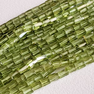 Può includere: Primo piano di fili di perline rettangolari verde chiaro. Le perline sono di dimensioni e forma uniformi, con un aspetto leggermente traslucido. Le perline sono disposte in file parallele, creando una superficie strutturata.