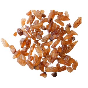 May include: A pile of small, rough, brown and orange crystals. The crystals are scattered on a white background.