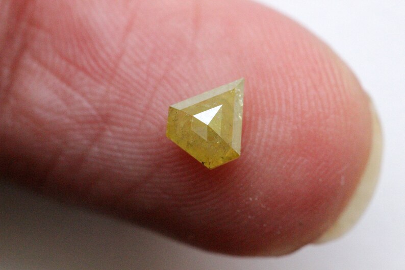 May include: A yellow diamond with a triangular shape, set on a finger.