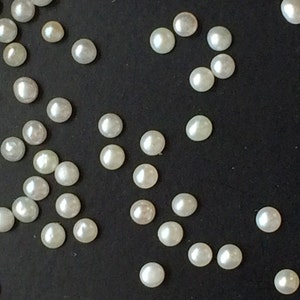 May include: A scattering of white pearl beads on a black surface.