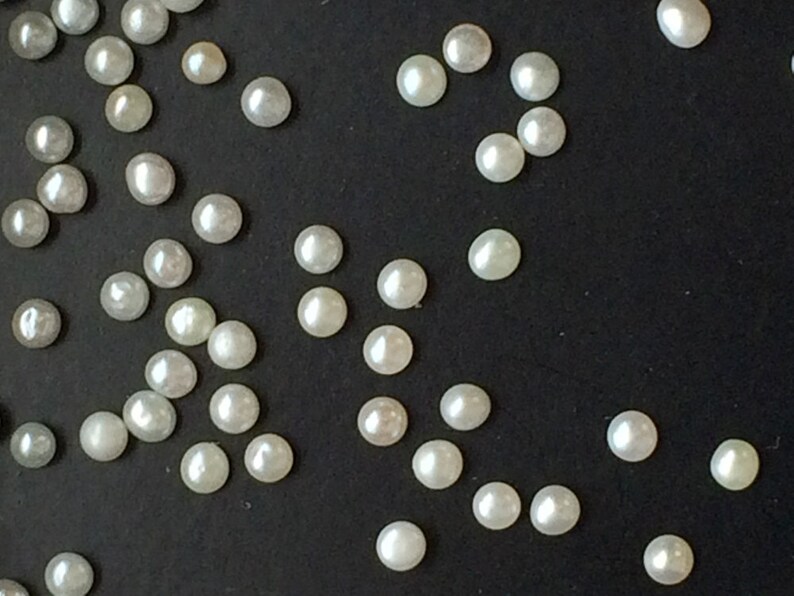 May include: A scattering of white pearl beads on a black surface.