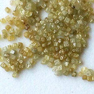 May include: A close-up of a pile of small, light green, faceted diamonds. The diamonds are scattered on a white surface.