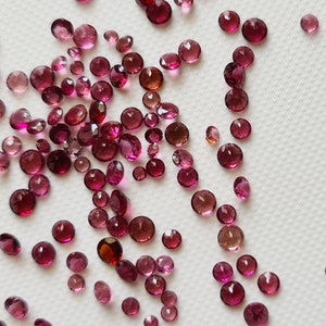 Op de afbeelding: Een verzameling ronde edelstenen in roze en rood, verspreid over een wit oppervlak.