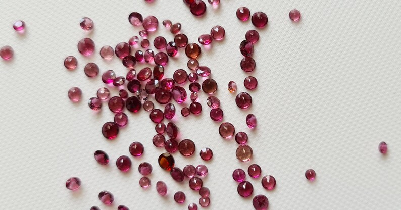 Op de afbeelding: Een verzameling ronde edelstenen in roze en rood, verspreid over een wit oppervlak.