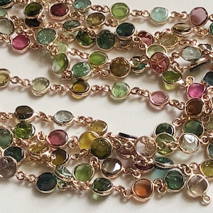 May include: A multi-strand necklace featuring a gold chain and round, faceted gemstones in shades of green, pink, and blue.