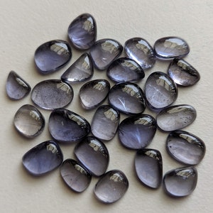 Peut inclure: Une collection de 25 pierres précieuses lisses, ovales, translucides, de couleur violet clair. Les pierres ont un léger éclat iridescent.