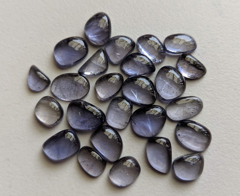 May include: A collection of 25 smooth, oval-shaped, translucent, light purple gemstones. The stones have a slightly iridescent sheen.