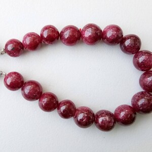 May include: A strand of deep red gemstone beads, each bead is round and smooth. The beads are strung on a cord with tassels at each end.