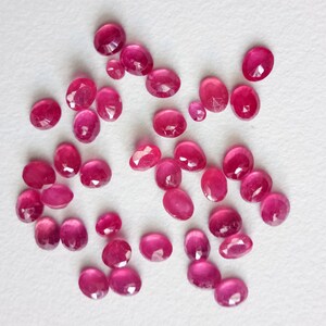 May include: A collection of oval-shaped, pink gemstones. The gemstones are various sizes and have a faceted cut.