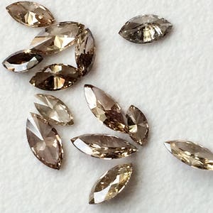 May include: A collection of marquise-shaped brown diamonds, some with a more golden hue, arranged on a white surface.