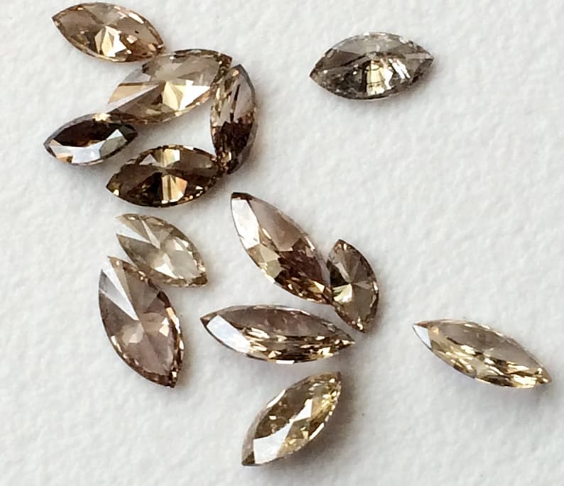 May include: A collection of marquise-shaped brown diamonds, some with a more golden hue, arranged on a white surface.