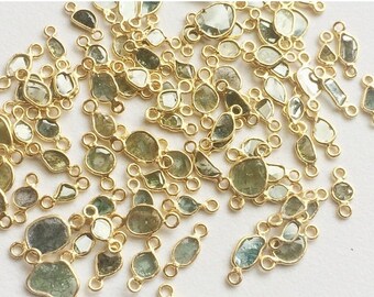 May include: A collection of green gemstone connectors with gold-toned metal accents. The gemstones are various shapes and sizes, including oval, round, and rectangular. The connectors are perfect for jewelry making.