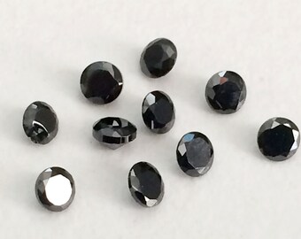 May include: Ten black round gemstones with a faceted cut. The gemstones are scattered on a white surface.