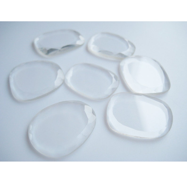 May include: Eight clear, smooth, and polished crystal stones in various shapes and sizes. The stones are arranged on a white surface.