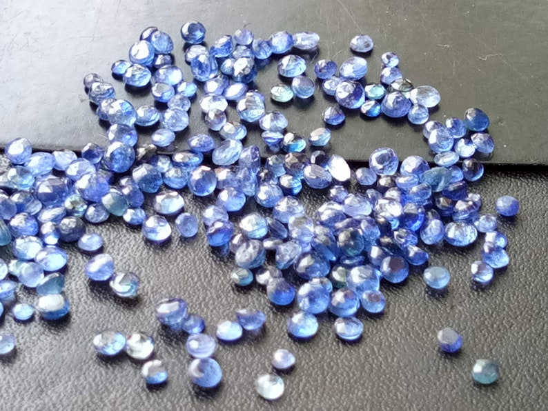 May include: A scattering of small, faceted, blue gemstones. The stones are oval-shaped and have a slightly irregular, natural appearance.
