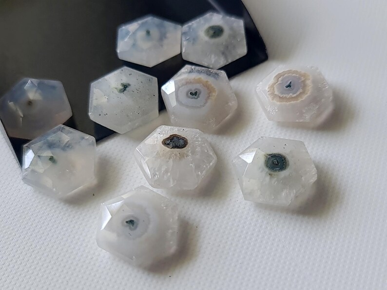 May include: Eight white, hexagonal, agate cabochons with green and brown inclusions. The cabochons are polished and have a smooth, glossy finish.