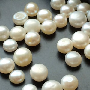 May include: A collection of white round pearls of various sizes, scattered on a dark surface.