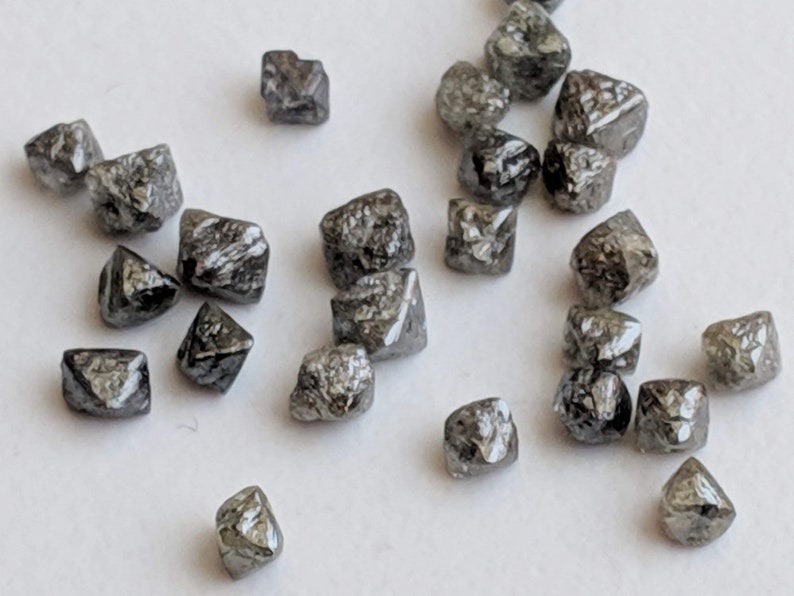 Puede incluir: Una colecci&oacute;n de peque&ntilde;os diamantes octa&eacute;dricos grises. Los diamantes est&aacute;n facetados y tienen un aspecto &aacute;spero y natural.