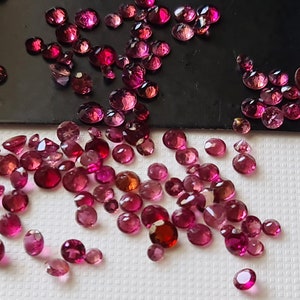 Op de afbeelding: Een verzameling losse roze edelstenen, sommige in een zwarte schaal en andere verspreid over een wit oppervlak.