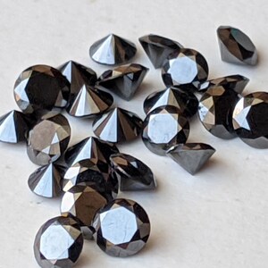 May include: A collection of black diamond gemstones, each with a faceted cut, arranged on a white surface.