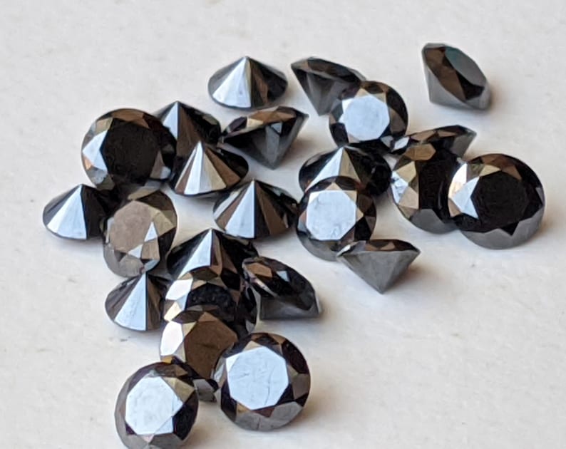 May include: A collection of black diamond gemstones, each with a faceted cut, arranged on a white surface.