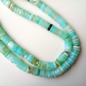 May include: A strand of light blue opal beads, with a slightly iridescent sheen. The beads are small and round, and they are strung on a clear thread.