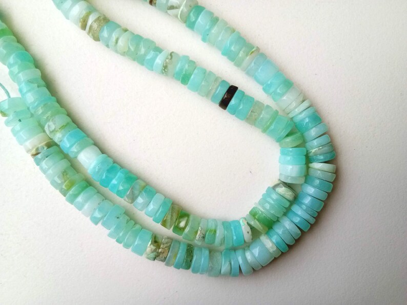 May include: A strand of light blue opal beads, with a slightly iridescent sheen. The beads are small and round, and they are strung on a clear thread.