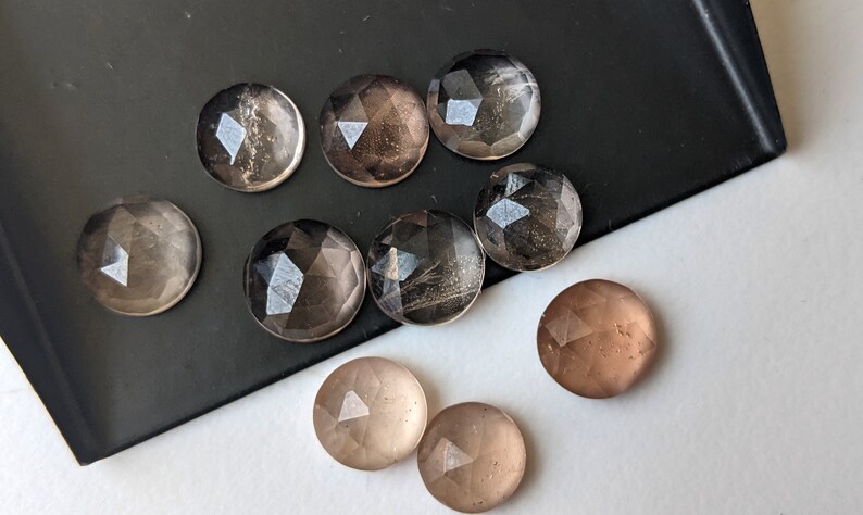 Puede incluir: Ocho cabujones redondos facetados de cuarzo transparente y ahumado. Los cabujones tienen un di&aacute;metro aproximado de 2,5 cm.