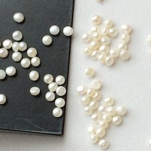 May include: A collection of white pearl beads, some on a black surface and some on a white surface.
