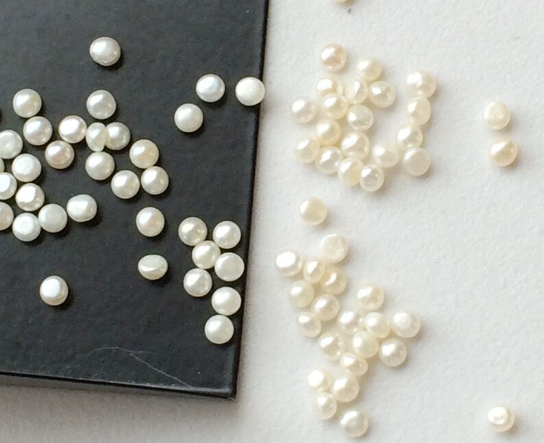 May include: A collection of white pearl beads, some on a black surface and some on a white surface.