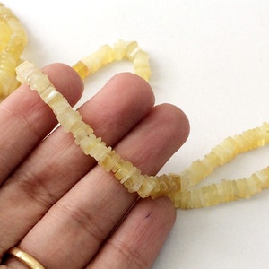 May include: A strand of pale yellow, square-shaped opal beads. The beads are strung on a clear thread and are approximately 1/2 inch in length.