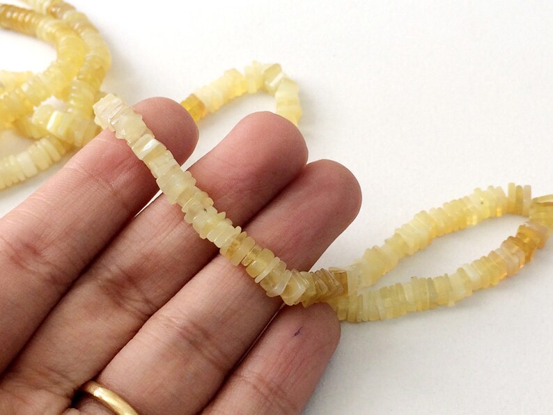 May include: A strand of pale yellow, square-shaped opal beads. The beads are strung on a clear thread and are approximately 1/2 inch in length.