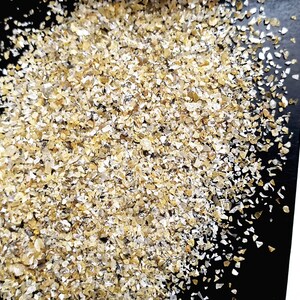 May include: A close-up of a pile of small, golden-brown flakes of rolled oats on a black surface.