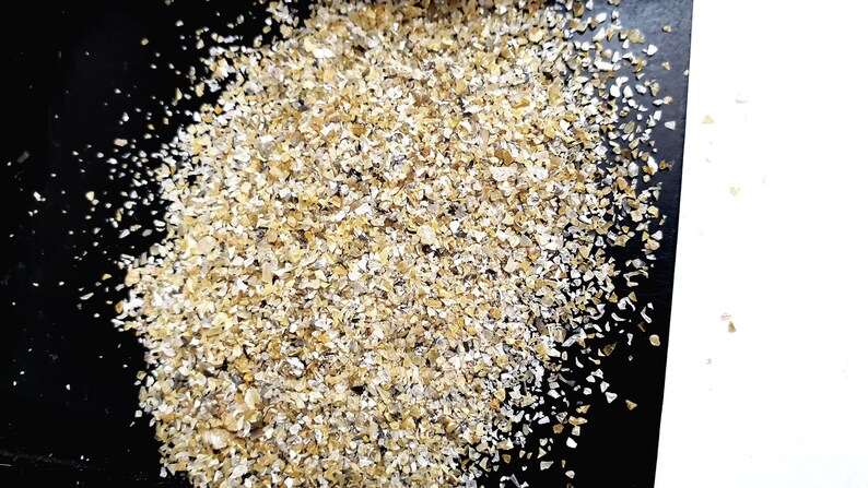 May include: A close-up of a pile of small, golden-brown flakes of rolled oats on a black surface.