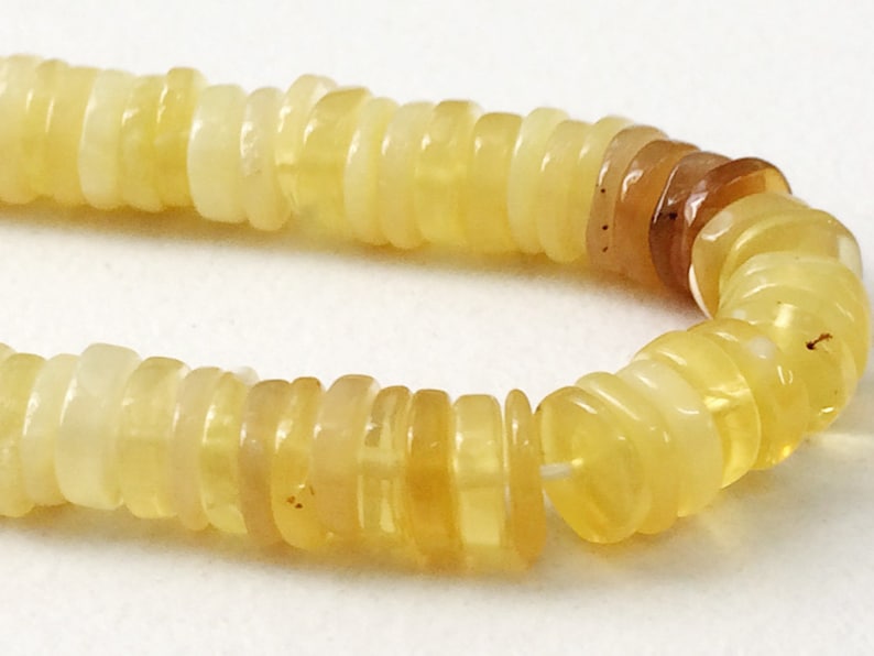 May include: A strand of yellow opal beads, each bead is made of stacked, thin, round discs. The beads are strung on a white thread.