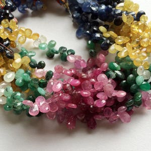 May include: A strand of gemstone beads in various colors, including blue, yellow, green, and pink. The beads are faceted and have a teardrop shape.