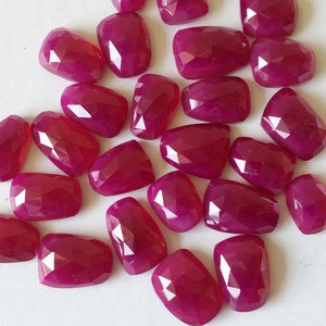 May include: A collection of 20 faceted, pink gemstone cabochons. The stones are all roughly the same size and shape, and they have a smooth, polished finish.