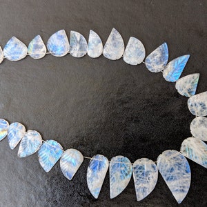 May include: A strand of iridescent white moonstone beads, each carved in a leaf shape. The beads are strung on a silver wire and have a blue and green iridescent sheen.