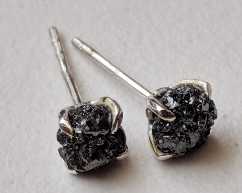 May include: A pair of silver stud earrings with black diamond accents. The diamonds are rough and have a natural, unpolished look.