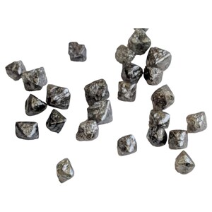 Puede incluir: Una colecci&oacute;n de peque&ntilde;os diamantes negros en bruto. Los diamantes est&aacute;n dispersos sobre un fondo blanco.