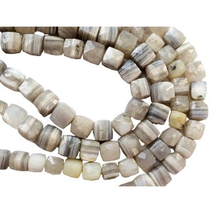 May include: A strand of gray and white agate beads with a faceted, square shape. The beads are strung on a clear thread.