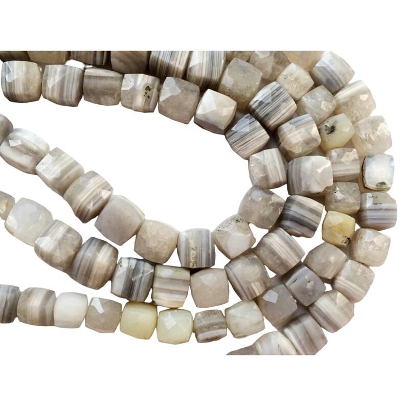 May include: A strand of gray and white agate beads with a faceted, square shape. The beads are strung on a clear thread.