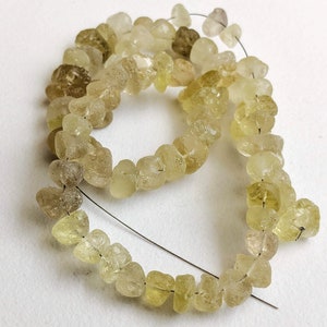 May include: A strand of light yellow and clear faceted gemstone beads. The beads are irregular in shape and have a rough, natural texture. The beads are strung on a thin wire.