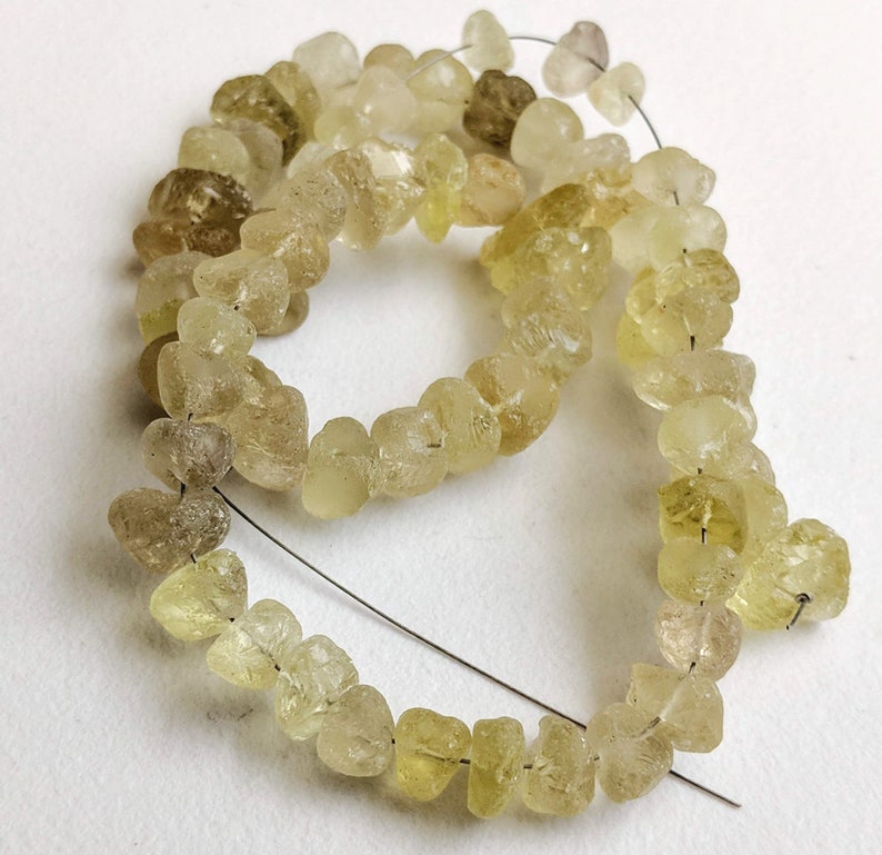 May include: A strand of light yellow and clear faceted gemstone beads. The beads are irregular in shape and have a rough, natural texture. The beads are strung on a thin wire.