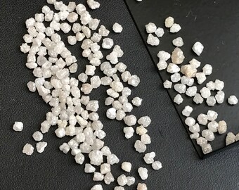 May include: A close-up of a collection of small, white, rough diamonds. The diamonds are scattered on a black surface.