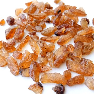 May include: A collection of small, rough, orange-brown gemstones. The stones are irregularly shaped and have a translucent appearance.